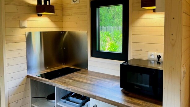 A compact kitchen with a built-in stove, microwave, and wooden cabinets. - ZEcamping 3 étoiles animaux acceptés locatif BBQ clim 4 pers (Neuilly-sur-Marne)