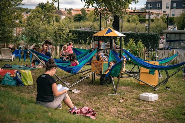 Un espace de jeux avec des hamacs et une petite structure, entouré d’herbe et d’arbres.