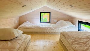 A cozy attic bedroom with two beds, wooden walls, and a window with a view of greenery. - ZEcamping 3 étoiles animaux acceptés locatif BBQ clim 4 pers (Neuilly-sur-Marne)