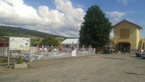 A hotel with a fenced pool area, a large tree, and a mountainous backdrop. - ZEcamping 3 étoiles piscine chauffée pet friendly mobil-home 5 pers (Lesperon)