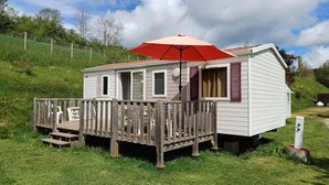 En campingvogn med træterrasse og rød parasol.