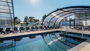 A swimming pool with lounge chairs and a covered area, surrounded by trees and buildings. - ZEcamping 4 étoiles familial espace aquatique mobil-home TV 35m2 (Guidel)