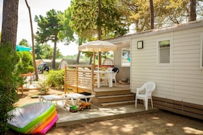 Una casa móvil con un patio que incluye una mesa y sillas, una zona de juegos pequeña con juguetes y una zona de estar cubierta.