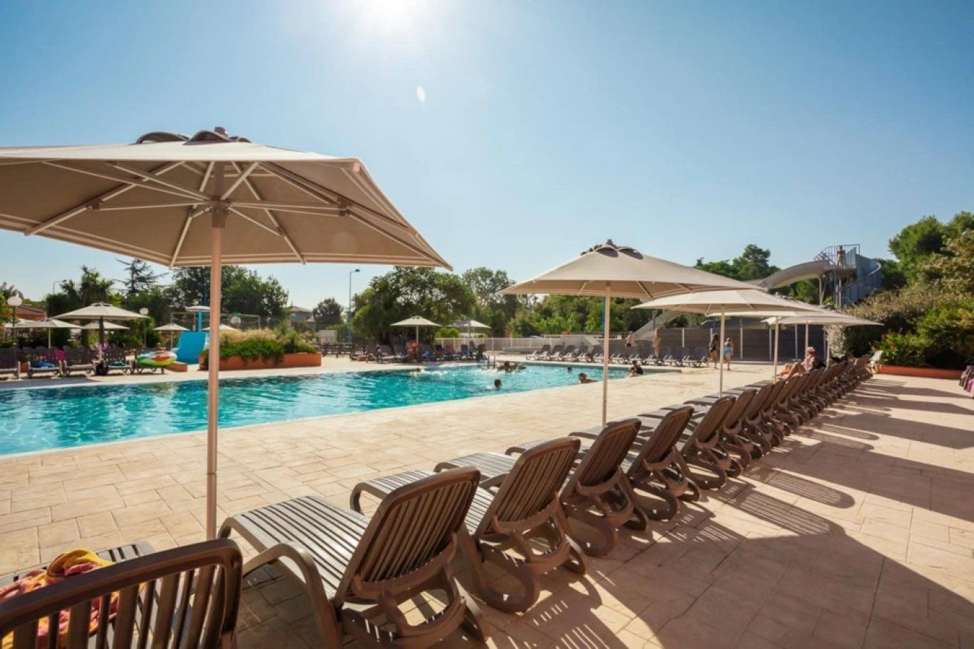 A poolside area with lounge chairs and umbrellas, a clear sky, and a pool.