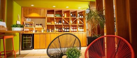 A bar area with wooden shelves stocked with bottles, two wicker chairs, and a small table with a plant.