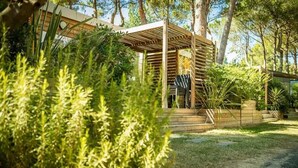 Um pátio moderno ao ar livre com pérgola de madeira, cercado por vegetação exuberante e árvores.
