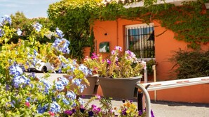 Um edifício com telhado de azulejos, uma janela com grade de metal e um vaso com flores.