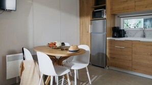 Une cuisine moderne avec des meubles en bois, un réfrigérateur en acier inoxydable, un four à micro-ondes et une machine à café. On y trouve une table à manger avec des chaises blanches et un saladier rempli de fruits.