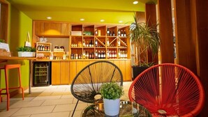 Un coin bar avec des étagères en bois remplies de bouteilles, deux fauteuils en osier et une petite table sur laquelle est posée une plante.