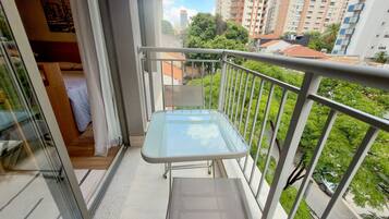 Uma varanda com mesa de vidro, corrimão de metal e vista para um horizonte urbano com edifícios e árvores.