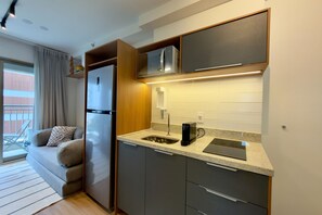 Eine kompakte Küche mit integriertem Kühlschrank, einer Kaffeemaschine und einer Mikrowelle.