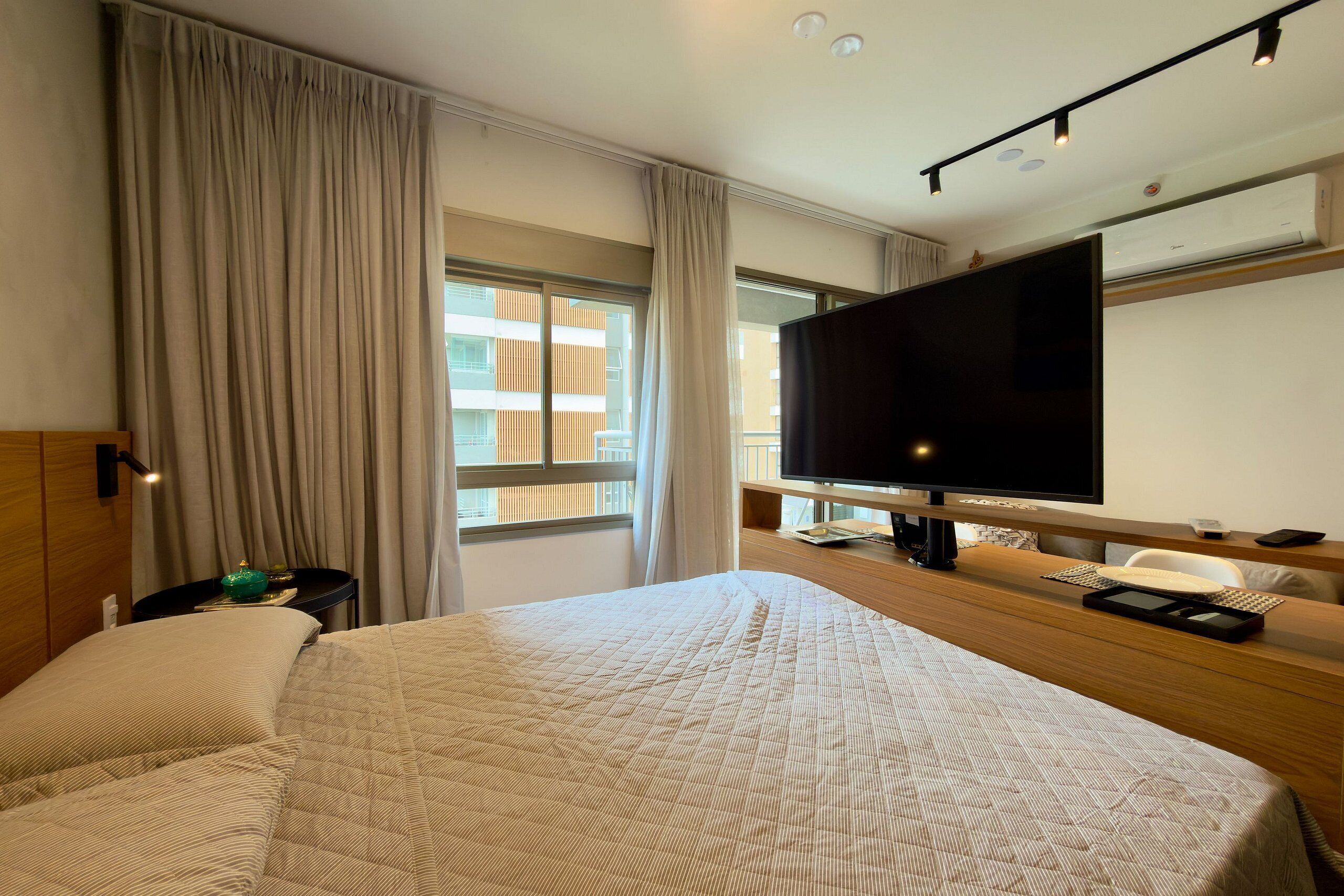 Ein Hotelzimmer mit einem großen Bett, einem Fernseher, einem Schreibtisch mit Stuhl und einem Fenster mit Vorhängen.