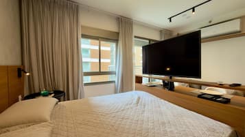 Habitación de hotel con una cama grande, un televisor, un escritorio con una silla y una ventana con cortinas.