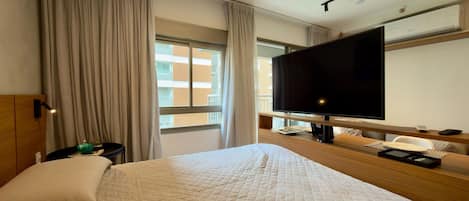 A hotel room with a large bed, a TV, a desk with a chair, and a window with curtains.