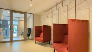 Een moderne lobby met glazen deuren, een zithoek met rode fauteuils en een vloer van witte tegels.