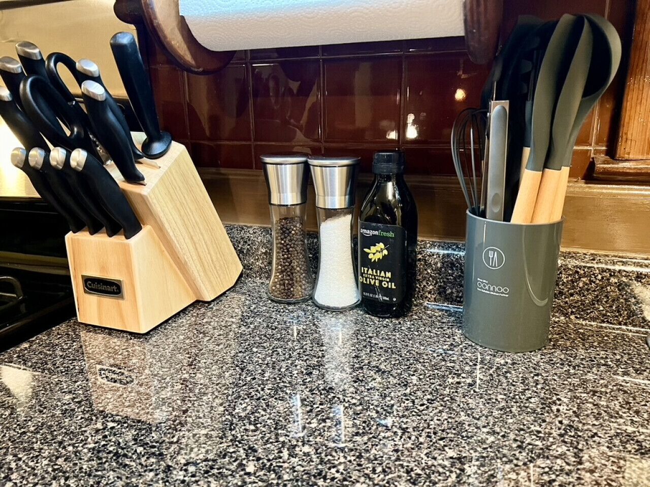 A kitchen counter with a knife block, salt and pepper shakers, a bottle of olive oil, and a utensil holder.