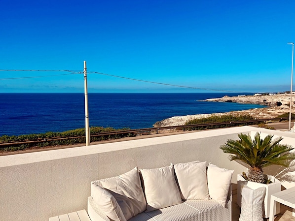 A seaside terrace with a white sofa and a potted plant, overlooking a rocky coastline and the sea. - Villetta Costa Azure - Con Piscina Vista Mare (Castrignano del Capo)