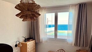 A bedroom with a bed, a dresser, a wicker chair, a small table, and a window with a view of the ocean. - Villetta Costa Azure - Con Piscina Vista Mare (Castrignano del Capo)