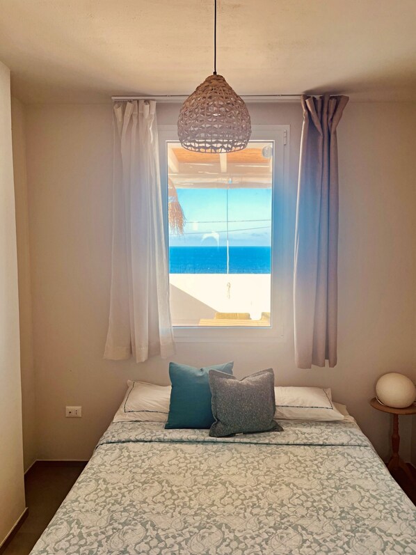 A bedroom with a bed, a hanging light fixture, a window with curtains, and a view of the sea. - Villetta Costa Azure - Con Piscina Vista Mare (Castrignano del Capo)