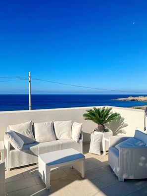 A terrace with a white wicker sofa, a matching ottoman, and a small table, overlooking a clear blue sea and rocky coastline. - Villetta Costa Azure - Con Piscina Vista Mare (Castrignano del Capo)