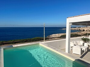 A pool with clear blue water, a white outdoor seating area with white wicker furniture, and a view of the sea and rocky coastline. - Villetta Costa Azure - Con Piscina Vista Mare (Castrignano del Capo)