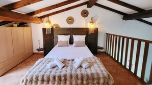 Ein Schlafzimmer mit Holzboden, einem Bett mit weißer Bettwäsche, zwei Wandleuchten und einem Holzbalken.