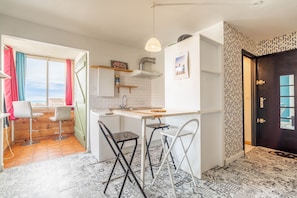 A compact kitchen with a dining area, a window with curtains, a patterned floor, and a dark door.