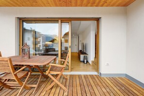 A wooden deck with a table and chairs, a sliding glass door leading to an interior space, and a view of a mountain. - Rostrini Family Home Alpine Retreat with Mountain View (Cavalese)