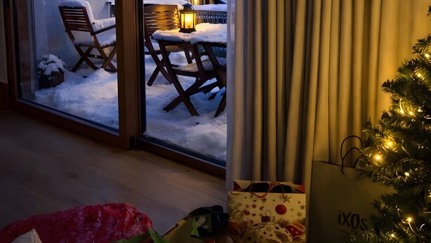 Quarto com vista para montanhas cobertas de neve, uma cadeira de madeira, uma mesa com um candeeiro e um pinheiro de Natal.