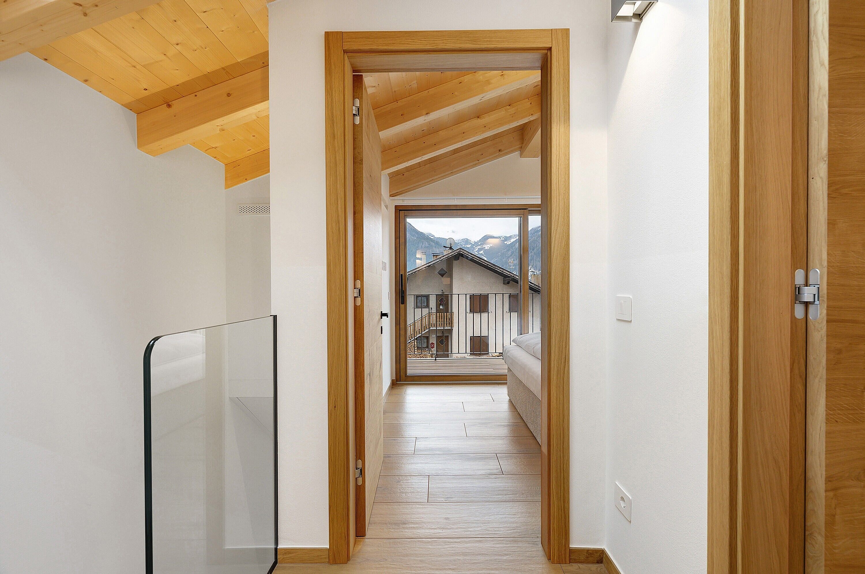 Un corridoio stretto con travi in legno, una ringhiera in vetro e vista su un edificio con un balcone.