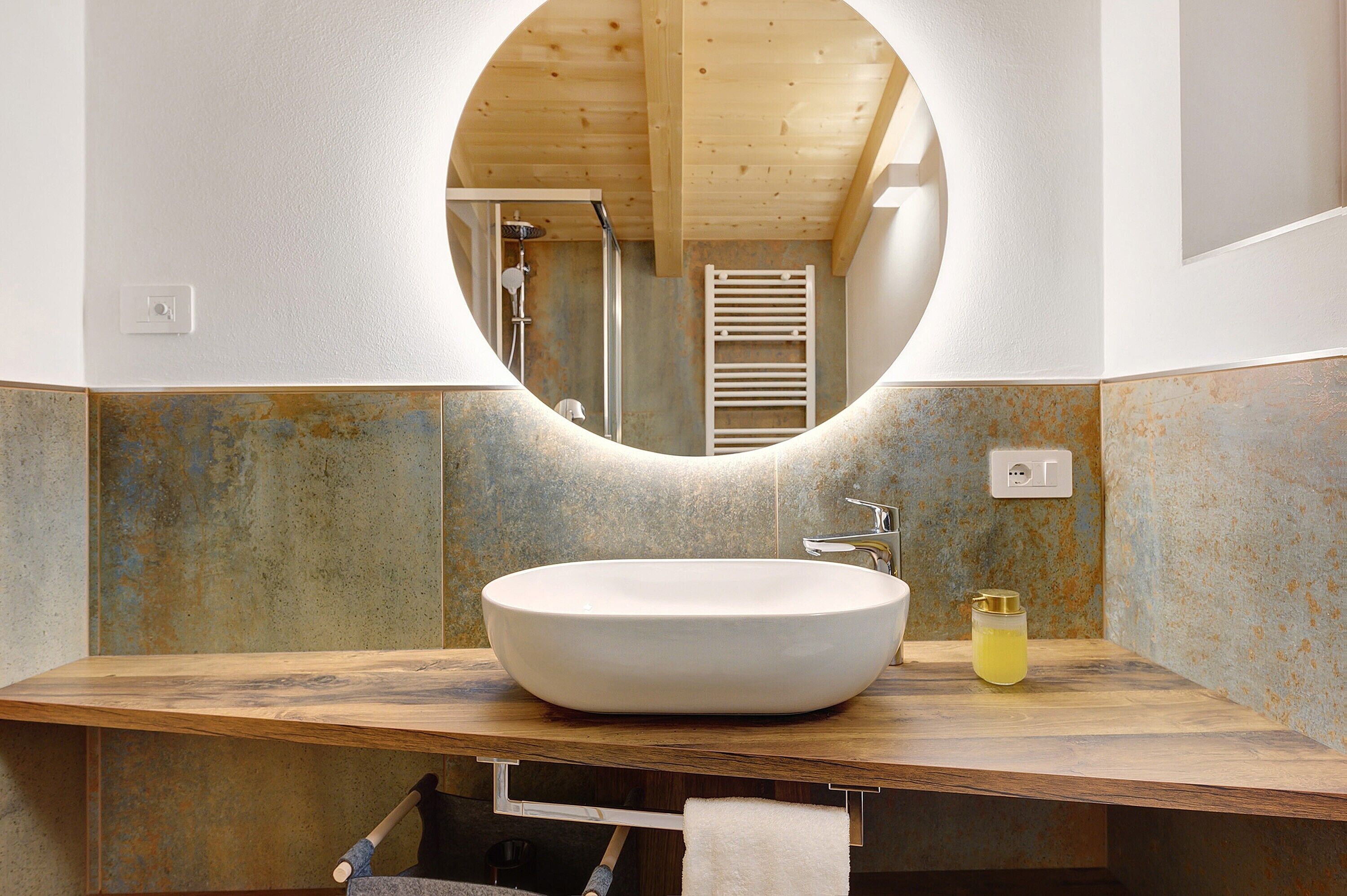A bathroom with a round mirror, a wooden vanity, a white sink, and a towel rack.