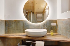 A bathroom with a round mirror, a wooden vanity, a white sink, and a towel rack. - Rostrini Family Home Alpine Retreat with Mountain View (Cavalese)
