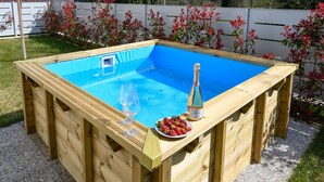 A wooden pool with a blue interior, a bottle of champagne, and a plate of strawberries.