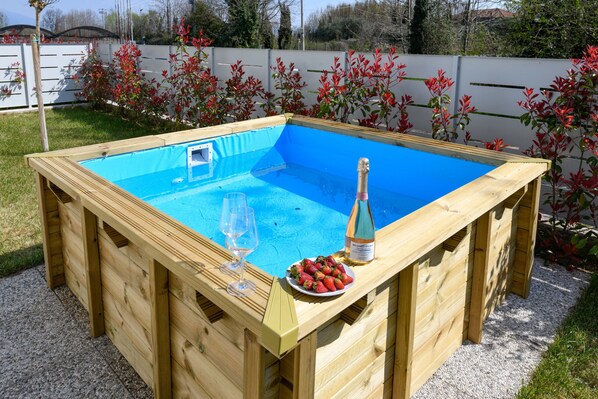 Ein hölzerner Pool mit blauer Innenauskleidung, eine Champagnerflasche und ein Teller Erdbeeren.
