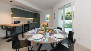 A modern kitchen with dark cabinets, a microwave, and a sink. There is a dining table set with plates, cups, and a vase of flowers.