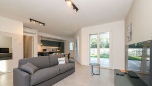 A modern living room with a grey sofa, a flat-screen TV, and a dining area with a table and chairs.