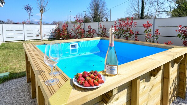 A wooden pool table with a blue pool, a bottle of champagne, and a plate of strawberries.