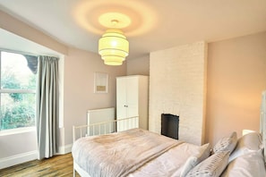 Une chambre à coucher avec un lit, un radiateur, une armoire, une cheminée et une fenêtre avec des rideaux.