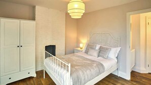 Een slaapkamer met een wit bed, een witte kledingkast, een witte wand en een houten vloer.