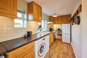 Eine kleine Küche mit Holzausstattung, einer Waschmaschine, einem Kühlschrank und einer Mikrowelle.