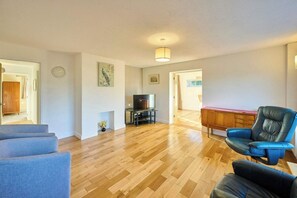 Ein geräumiges Wohnzimmer mit Holzboden, einem blauen Sofa, einem Ledersessel, einem Fernseher und einem Holzkabinett.