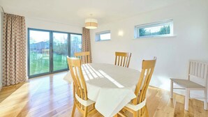 Ein Esszimmer mit großem Tisch und Stühlen, einer Schiebetür zum Garten und einer Deckenleuchte.
