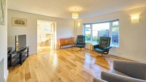 Ein geräumiges Wohnzimmer mit Holzböden, einem Fernseher, zwei Ledersesseln und einem grauen Sofa.