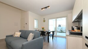 Ein modernes Wohnzimmer mit einem grauen Sofa, einem Essbereich mit Tisch und Stühlen sowie einer Küche mit Arbeitsplatte.