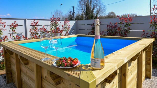 Ein Holzbadefass mit einem blauen Pool, einem Glas Wein und einer Schale Erdbeeren.