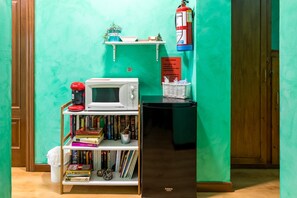 Eine Küche mit Mikrowelle, Bücherregalen, einer kleinen Ablage mit Dekoration, einem Feuerlöscher und einem Kühlschrank.