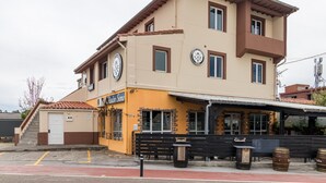 Un bâtiment à deux étages, doté d’un toit plat, d’une enseigne indiquant « Festa Sona » et d’un petit espace extérieur aménagé avec des bancs et des barils.