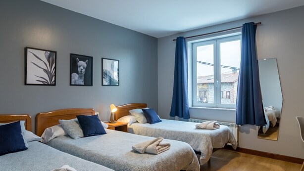 Une chambre d’hôtel avec deux lits, une fenêtre avec des rideaux, une lampe et des tableaux encadrés au mur.
