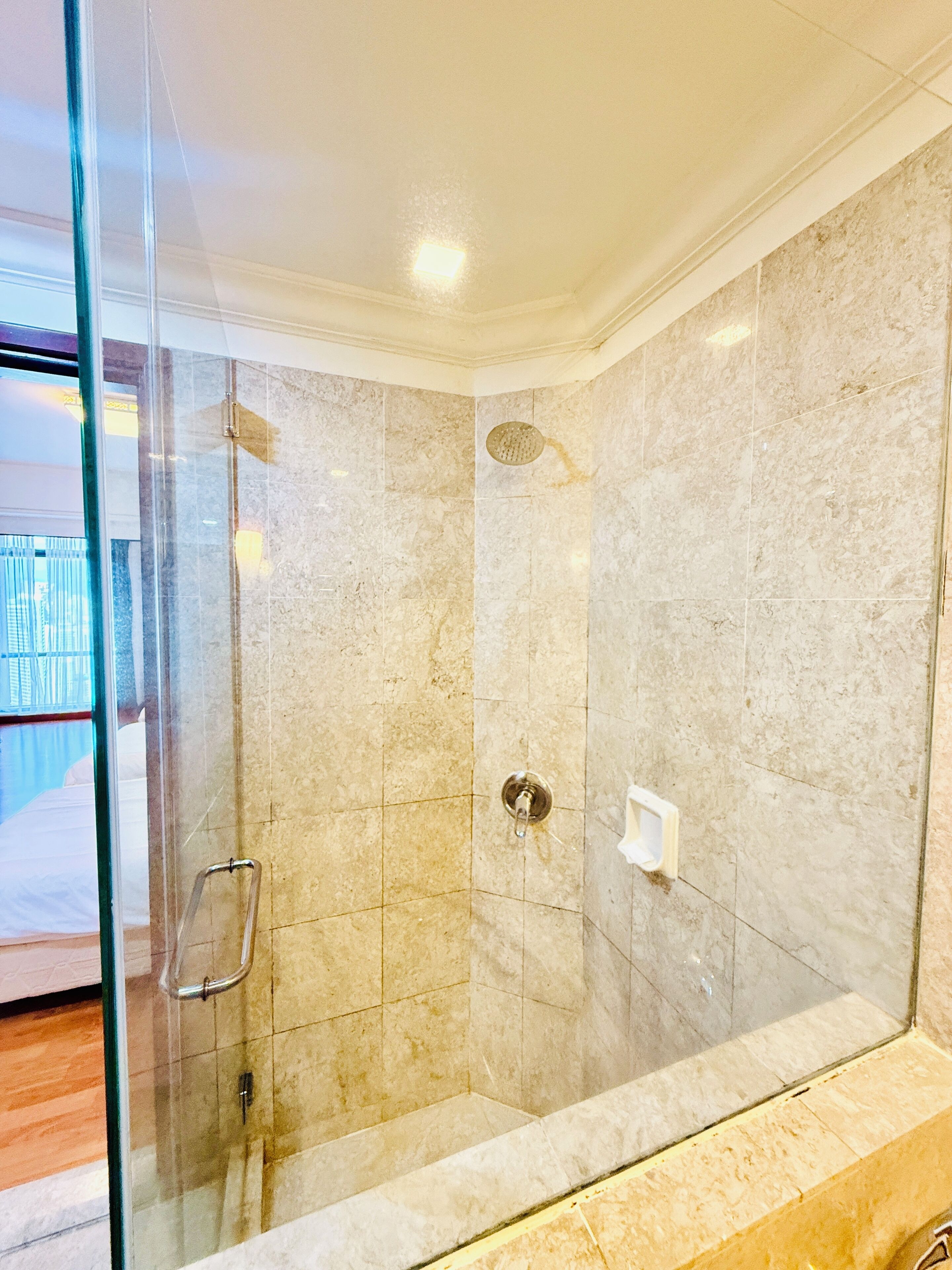A glass-enclosed shower with a handheld showerhead, a handheld showerhead, and a wall-mounted hand dryer.