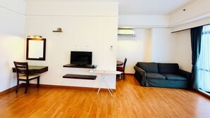 A modern living room with a flat-screen TV, a small desk, a chair, and a sofa. - Alpha Suite at times square  (Kuala Lumpur)